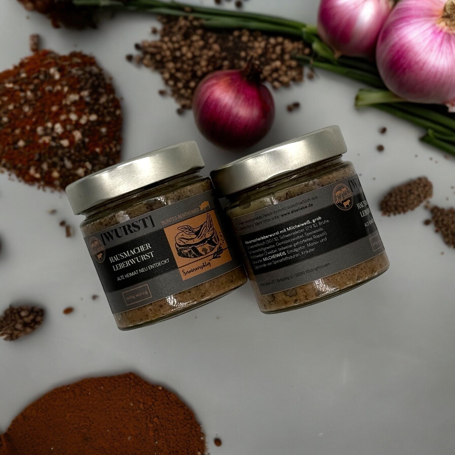 Ein Glas Leberwurst liegt auf einer Arbeitsplatte, dekoriert mit Gewürzen und Zwiebeln. Es ist die Sorte Hausmacher der Marke elseLiebe zu sehen.