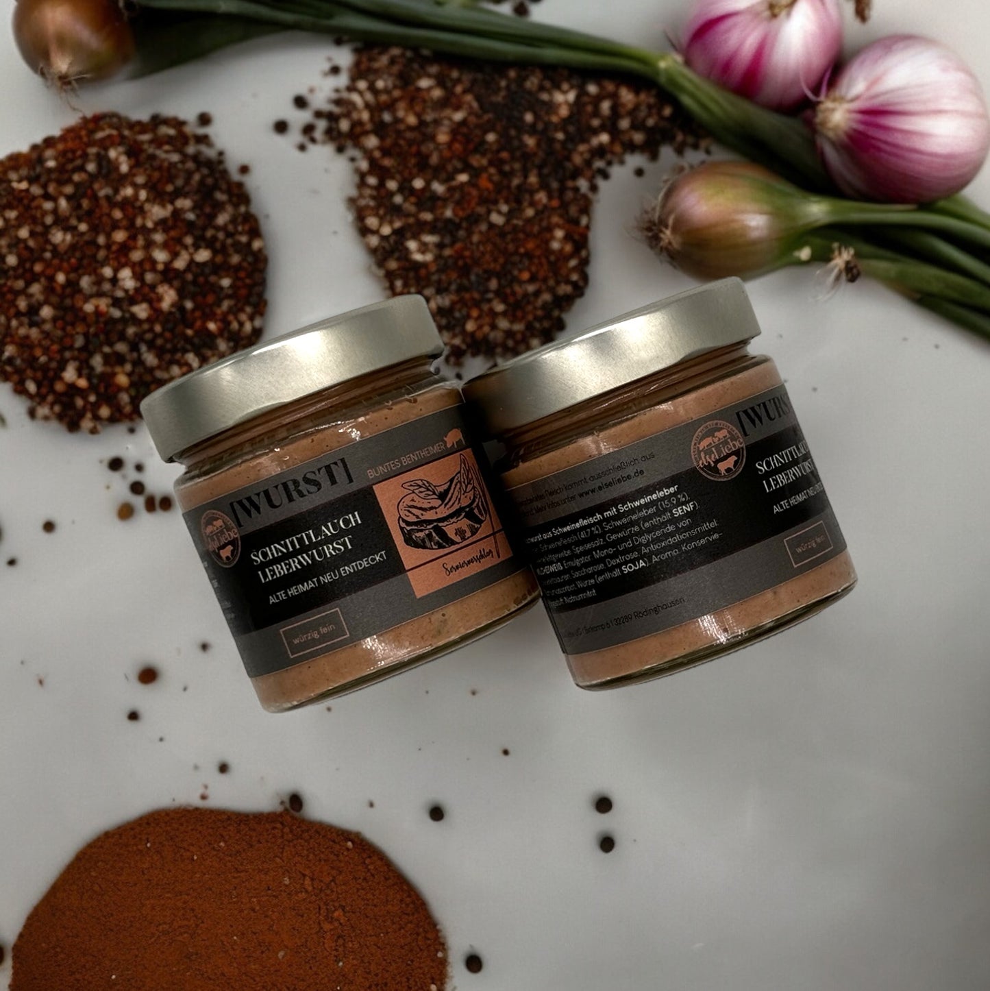 Ein Glas Leberwurst liegt auf einer Arbeitsplatte, dekoriert mit Gewürzen und Zwiebeln. Es ist die Sorte Schnittlauch der Marke elseLiebe zu sehen.